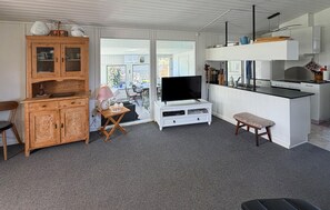 A compact living space with a wooden cabinet, a television on a white stand, a small table with a lamp, and a kitchen area with a stove and sink. - 2 bedroom nice home in Sydals (Sydals)