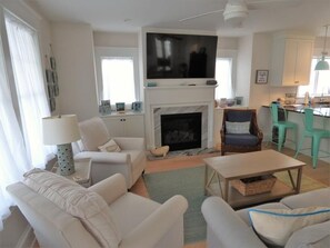 A living room with a fireplace, a television, and a dining area with chairs. - Ocean View Beach Block Condo | 4BR | Private Elevator | Large Deck | Sleeps 10 (Ocean City)