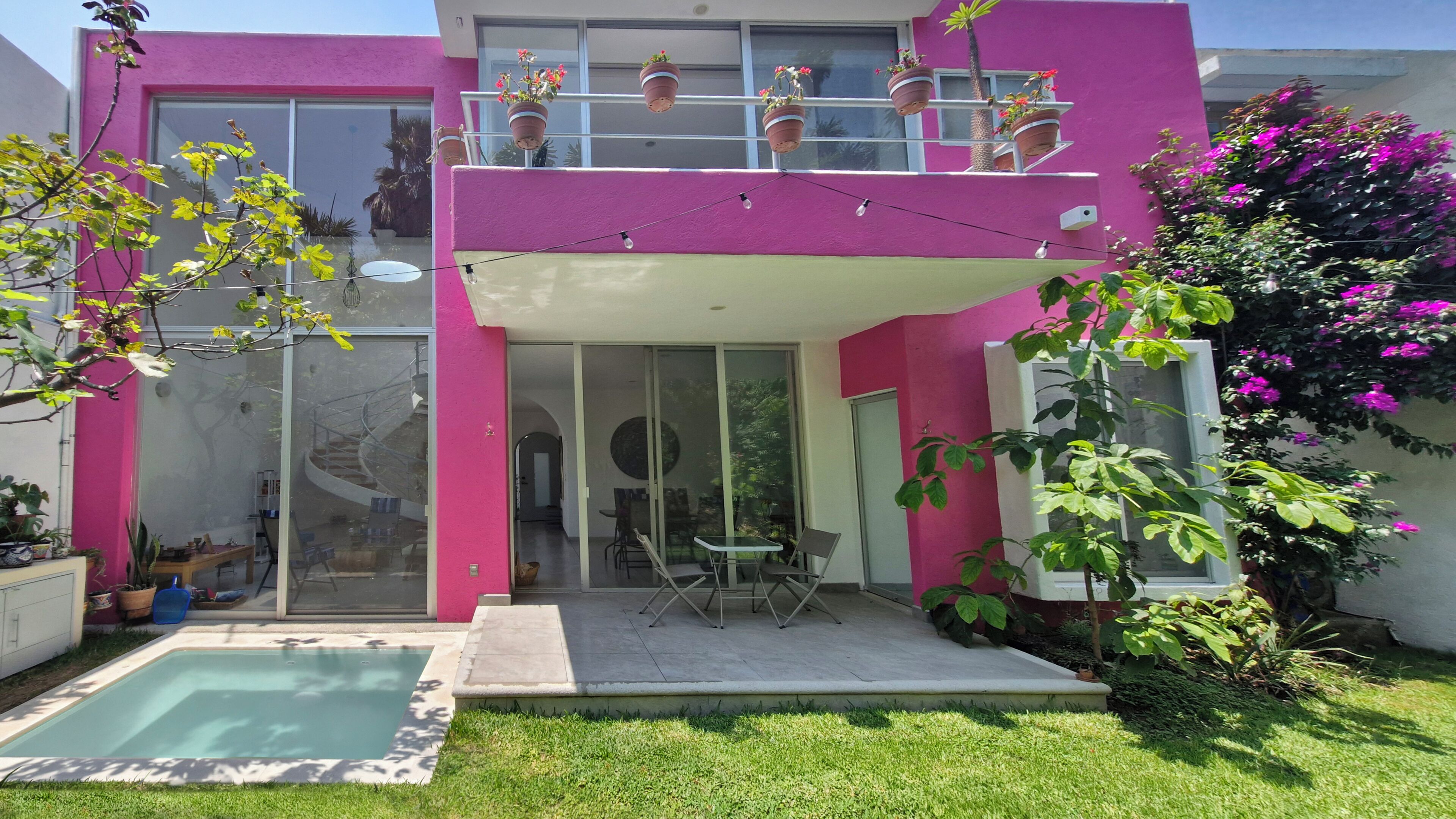 A modern two-story house with a glass entrance, a pool, and potted plants on the balcony.