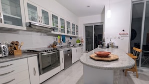 A modern kitchen with a central island, stainless steel appliances, and a dining area with a table and chairs. - Jardin Elvira (Cuernavaca)