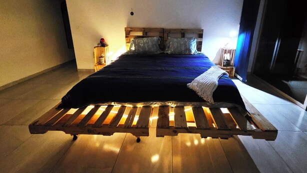 A bedroom with a wooden bed frame, a nightstand, and a window with a view. - Jardin Elvira (Cuernavaca)