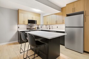 Eine moderne Küche mit Holzausstattung, einem Edelstahlkühlschrank, einer Mikrowelle und einem Barhocker.