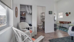 Ein Zimmer mit Korbmöbel, einem weißen Kleiderschrank, einem kleinen Badezimmer und Blick ins Freie.