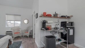 Ein gemütlicher Raum mit Küchenzeile, zwei Korbstühle, einem kleinen Tisch, einem Fenster und einem Spiegel.