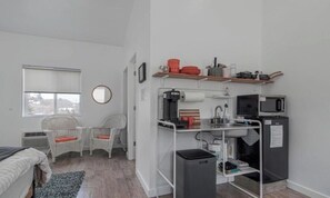 Et kompakt værelse med tekøkken, et lille spiseområde med fletstole, et vindue og et spejl.