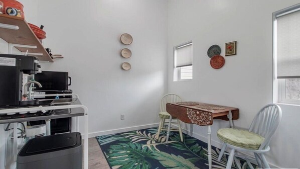 Une pièce compacte comprenant un coin cuisine, une petite table à manger, une chaise, une poubelle et une fenêtre.