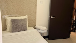 Ein Hotelzimmer mit Bett, Marmorwand, Tür und einem kleinen Tisch mit einem Handtuch.