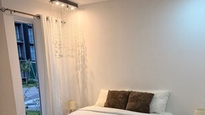Ein Schlafzimmer mit einem großen Bett, einer Chandelüster, einem Fenster mit Vorhängen und einem Nachttischchen mit einer Lampe.