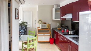 Een kleine keuken met rode kastjes, een magnetron en een eethoek met een groene stoel.