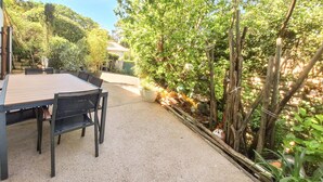 En udendørs patio med et bord og stole, omgivet af frodig vegetation og et træhegn.