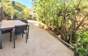 An outdoor patio with a table and chairs, surrounded by dense foliage and a wooden fence. - Lovely home in Arcachon with WiFi (Arcachon)