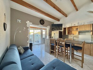 Eine moderne Küche mit Holzschränken, ein Essbereich mit Tisch und Stühlen sowie ein Wohnzimmer mit einer Couch.