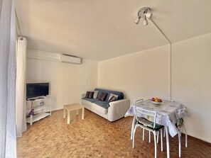 Ein kleines Wohnzimmer mit einer Couch, einem Fernseher, einem Tisch mit Stühlen und einem Fliesenboden.