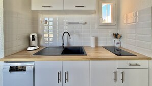 Una cocina con armarios blancos, un lavamanos negro, una cafetera y un ventanal.