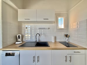 A kitchen with white cabinets, a black sink, a coffee maker, and a window. - CAP D'AGDE - Plage de la Roquille // Réf 0321 (CAP D'AGDE)
