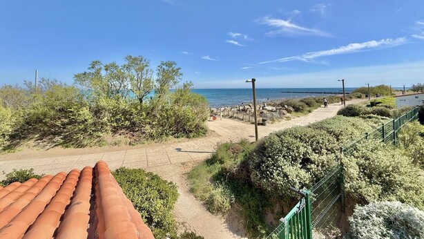 Un sendero costero con vegetación, cielo despejado y una vista distante del mar.