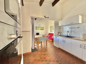 Una cocina moderna con armarios blancos, un comedor con sofá rojo y piso de baldosas.