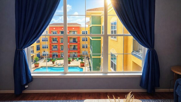 Quarto com uma janela grande, cortinas azuis e vista para edifícios coloridos, com uma piscina do lado de fora.