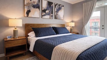 A bedroom with a wooden headboard, a bed with dark and light bedding, two bedside lamps, and abstract wall art.