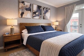 Une chambre à coucher avec une tête de lit en bois, un lit avec une literie aux couleurs sombres et claires, deux lampes de chevet et des œuvres d’art abstraites accrochées au mur.