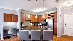 Uma cozinha moderna com uma ilha central, luminárias pendentes, armários de madeira e micro-ondas embutido.