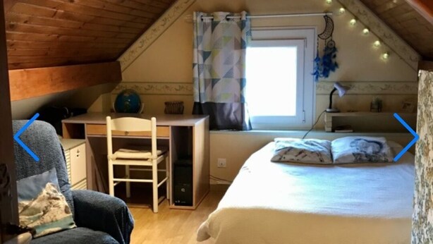 Une chambre mansardée chaleureuse, avec un plafond en pente, un lit, un bureau et une chaise.