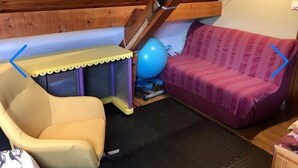 Une pièce avec une chaise jaune, un canapé violet, un ballon d’exercice bleu et une petite table dont le bord est jaune.
