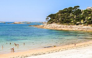 Une plage à l’eau claire, où l’on peut se baigner, et un rivage rocheux bordé d’arbres.