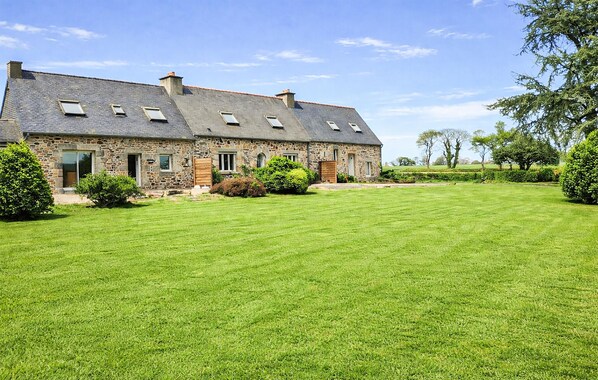 Une maison en pierre avec une grande pelouse, de nombreuses fenêtres et un ciel dégagé.