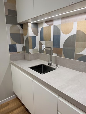 A kitchen with a sink, white cabinets, and a patterned backsplash.