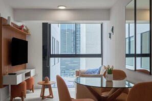 Ein modernes Wohnzimmer mit einem Flachbildfernseher, einem Glastisch, orangefarbenen Sessel und einem großen Fenster mit Blick auf die Stadt.