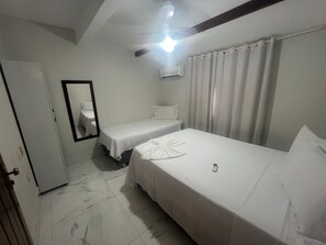 Quarto de hotel com duas camas de solteiro, ventilador de teto, ar condicionado, espelho e porta.