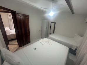 Quarto com duas camas, guarda-roupa, ventoinha no teto e espelho.