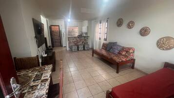 A living room with a sofa, a dining table, and a kitchen in the background.