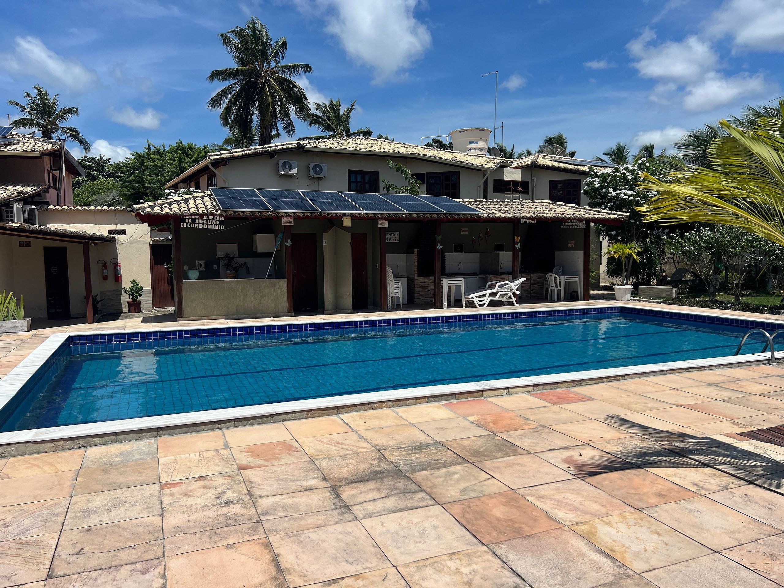 A swimming pool with a tiled deck, a building with a tiled roof, and a palm tree in the background.