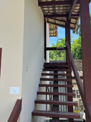 Escadaria com corrimão de metal que leva a uma área coberta, com vista para o verde lá fora.