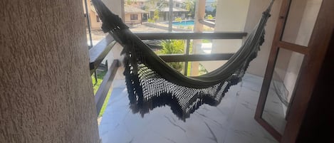 A hammock hanging between two pillars in a covered outdoor area with a view of a swimming pool and buildings in the background.