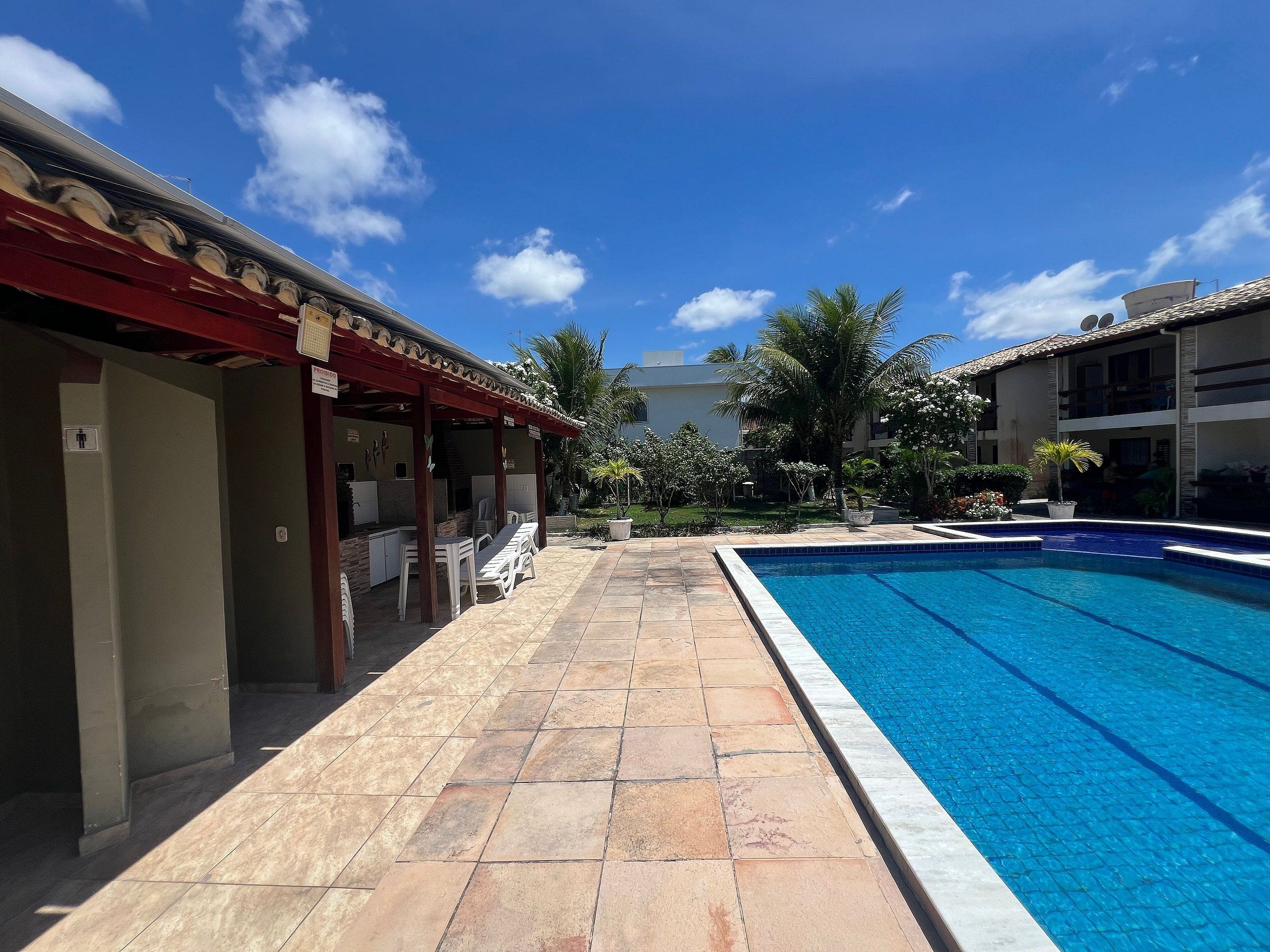 Piscina com deck revestido, área de estar externa e espaço coberto com mesas e cadeiras.