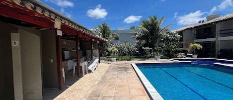 A swimming pool with a tiled deck, outdoor seating, and a covered area with tables and chairs.