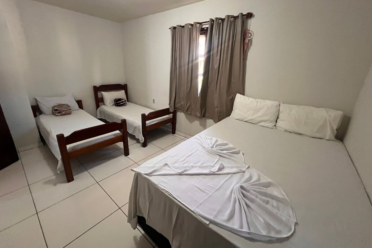 Una habitación con dos camas individuales y una cama doble, todo con ropa blanca.