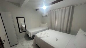 Een hotelkamer met twee bedden, een plafondventilator, een airconditioning en een spiegel, plus een deur.