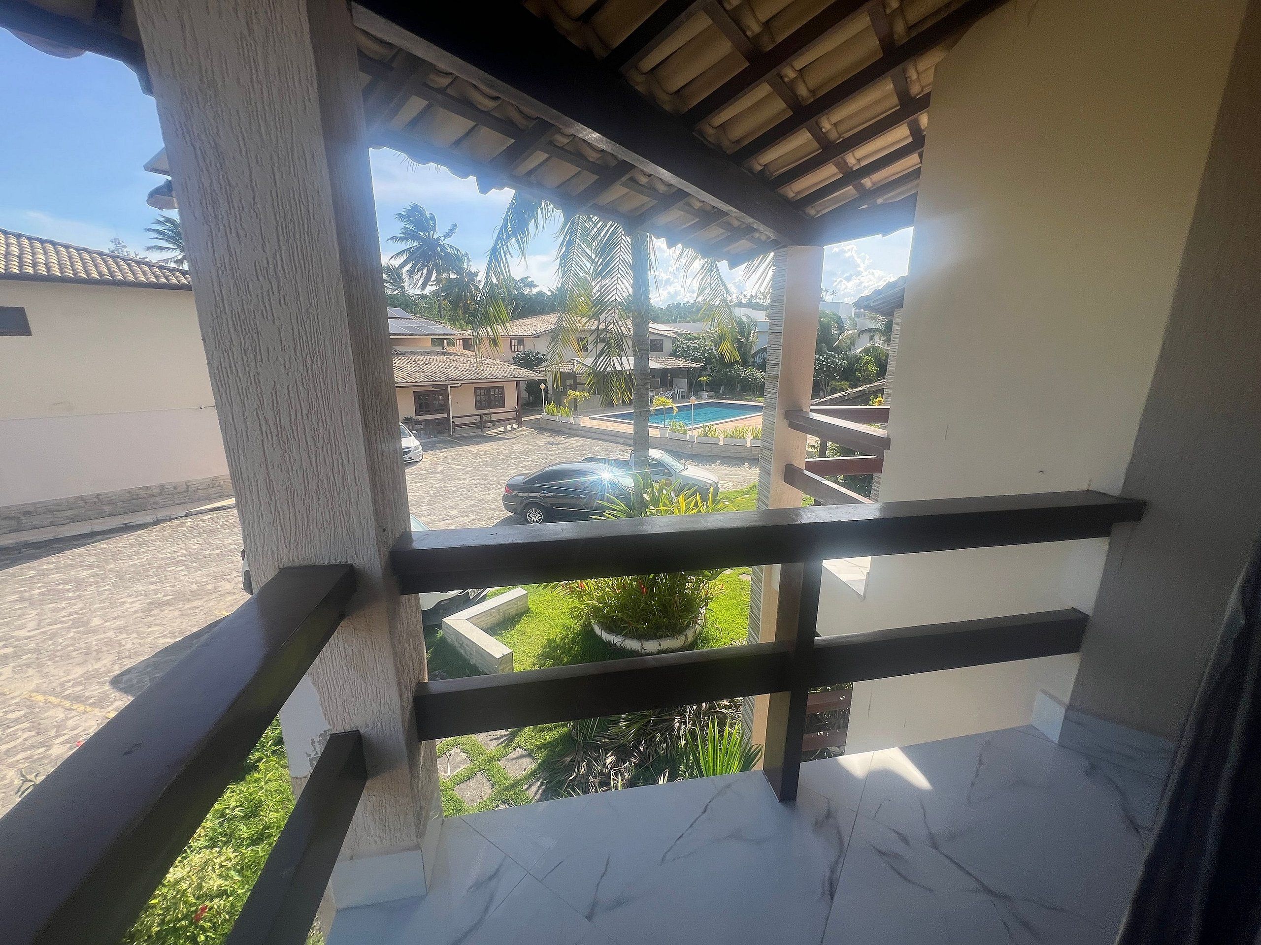 A balcony with a view of a swimming pool, palm trees, and residential buildings.
