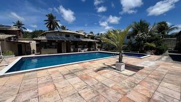 A swimming pool with tiled flooring, a palm tree, and a building with a tiled roof.