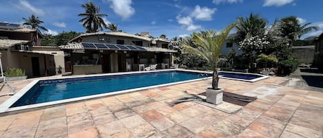 Una piscina con suelo de baldosas, una palmera y un edificio con tejado de tejas.