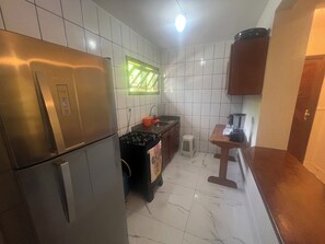 A compact kitchen with a refrigerator, stove, sink, and a small countertop with a blender. - Residencial Ouro Preto  (Porto Seguro)