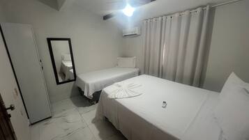Ein Hotelzimmer mit zwei Einzelbetten, einem Deckenventilator, einer Klimaanlage, einem Spiegel und einer Tür.