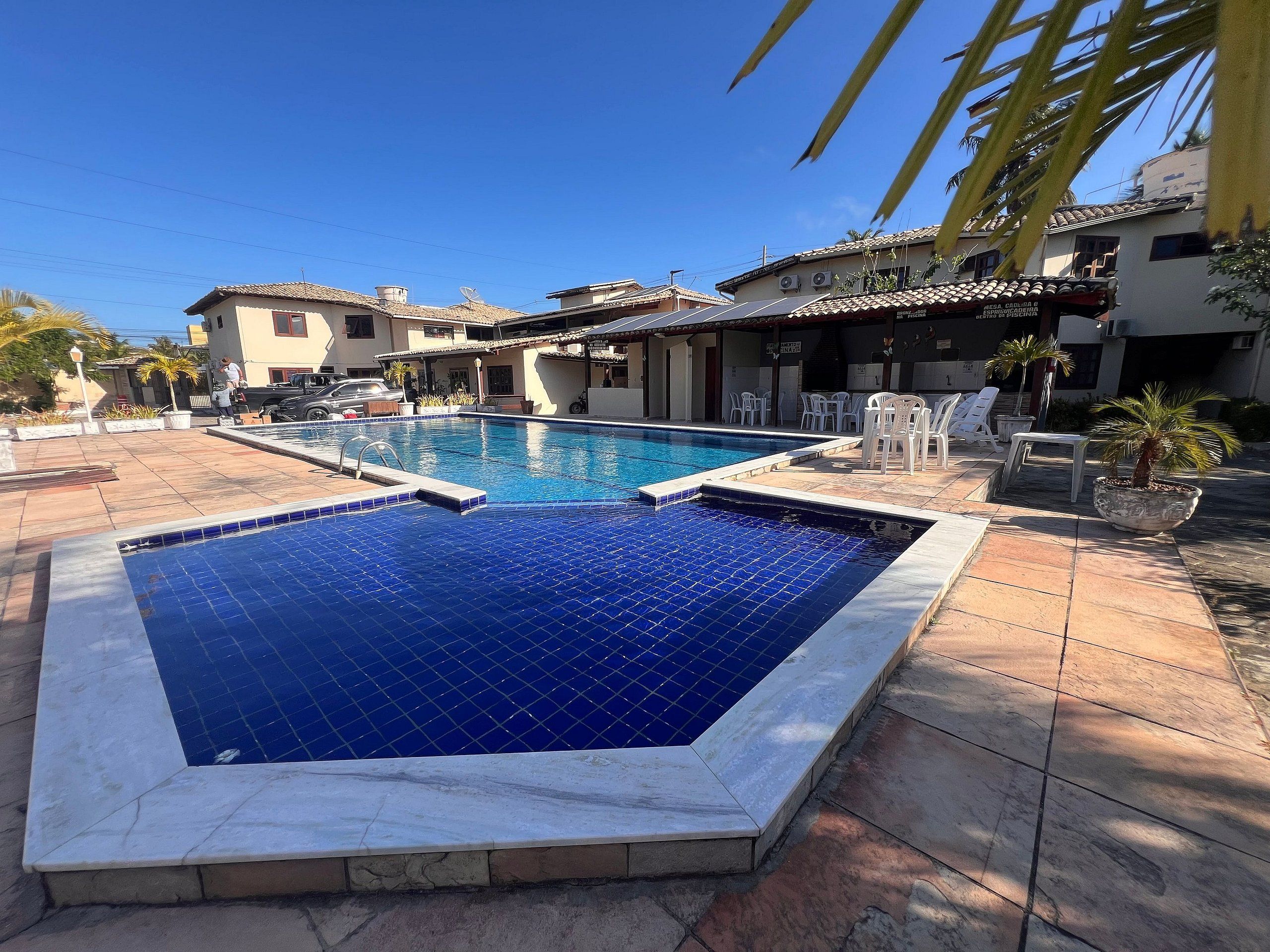 A swimming pool with tiled edges, surrounded by outdoor seating and palm trees.