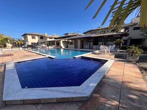 A swimming pool with tiled edges, surrounded by outdoor seating and palm trees. - Residencial Ouro Preto  (Porto Seguro)