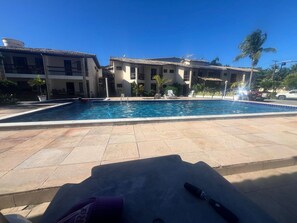 Piscina com deck azulejado, rodeada por edifícios com várias janelas e varandas.
