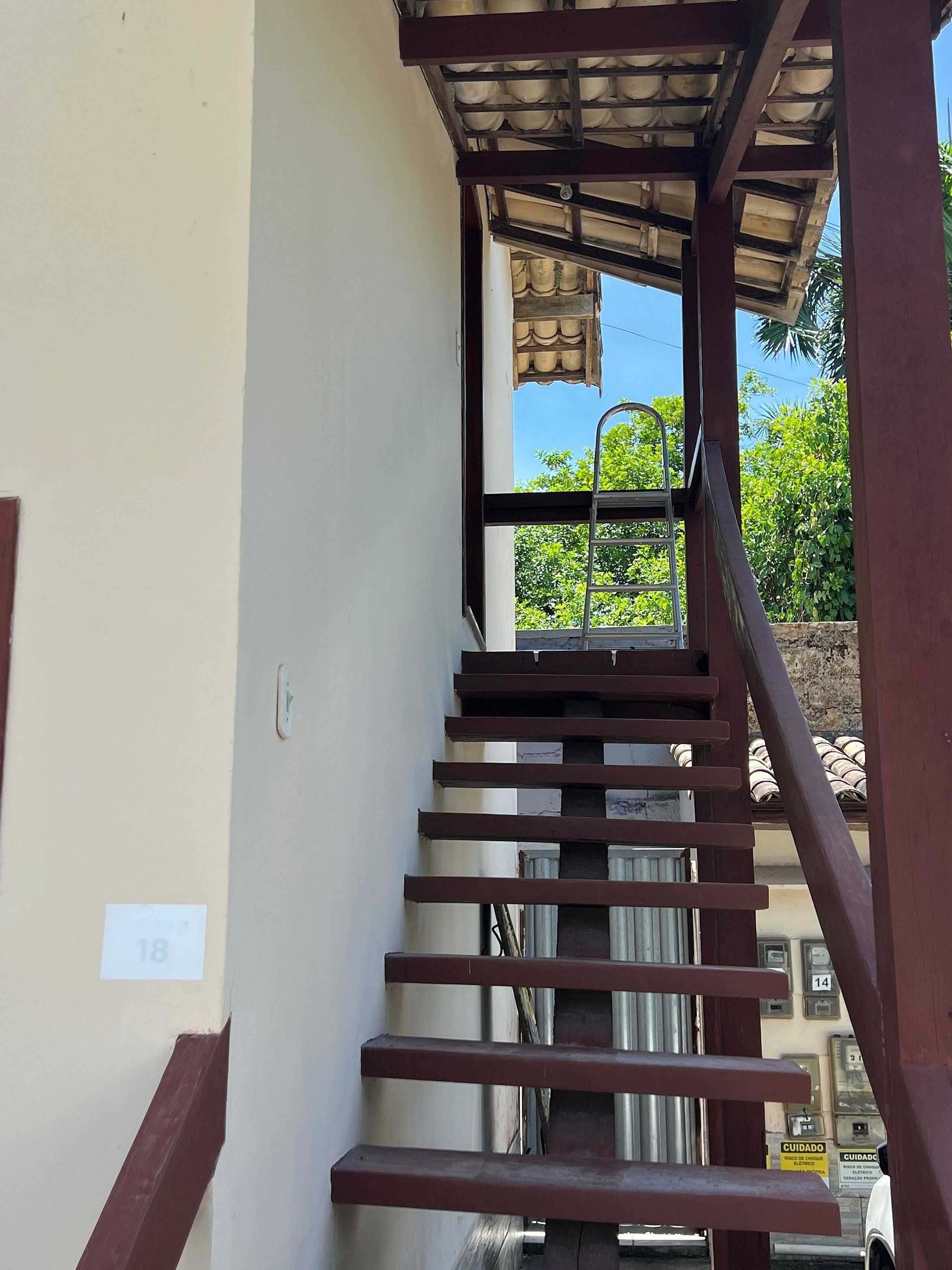A staircase with a metal handrail leading to a covered area with a view of greenery outside.